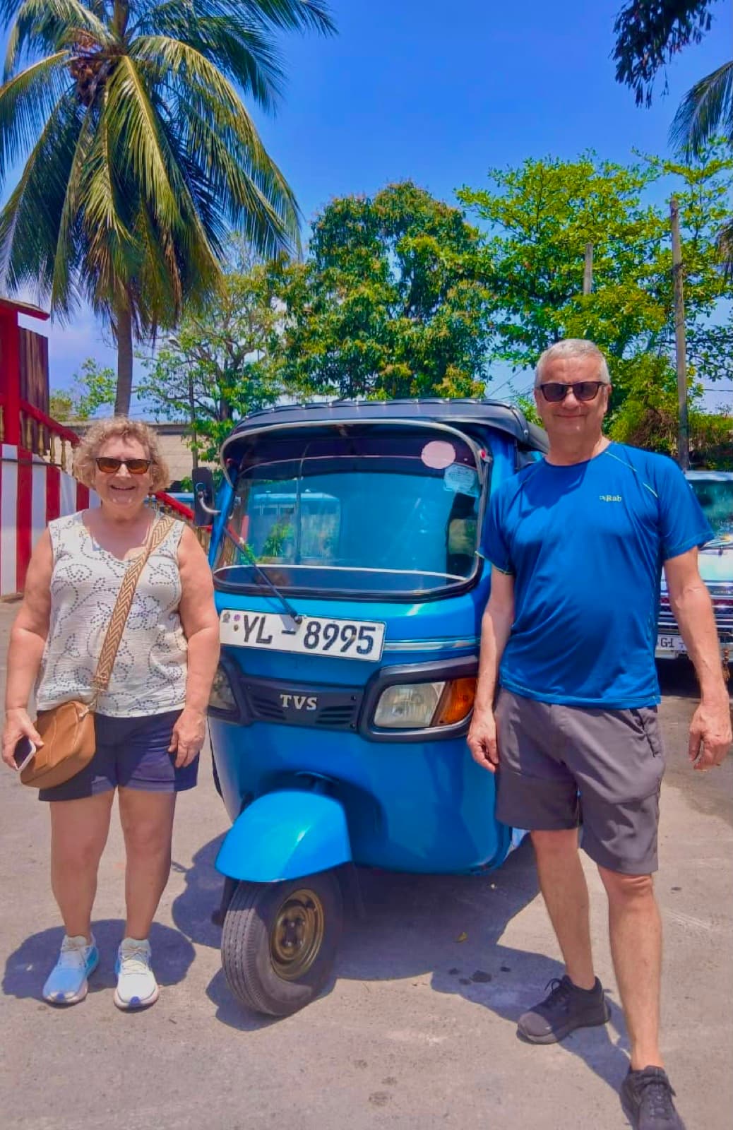 Couple beside David's blue tuk-tuk under the palms