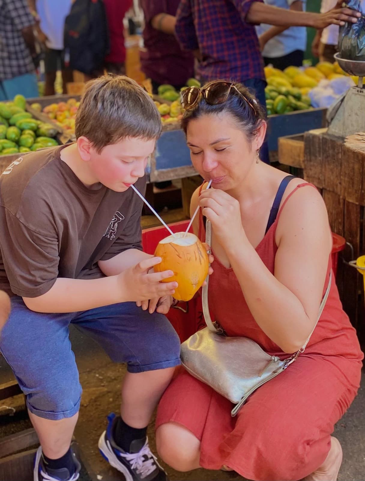 Mother and son sipping king coconut at a fruit market